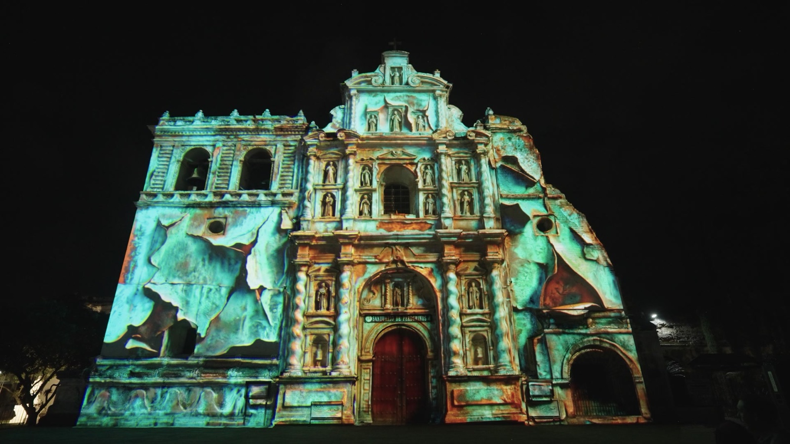 The baroque façade of the San Francisco church in La Antigua Guatemala at night, covered by RE:SORB’s projection mapping ‘Elemental Bodies’ in teal and orange, filmed during the Festival de la Luz 2026