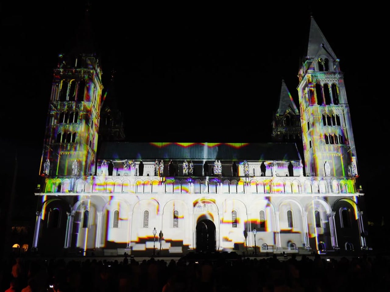 The towers of Pécs Cathedral in Hungary illuminated by a white and yellow 3D projection mapping at night